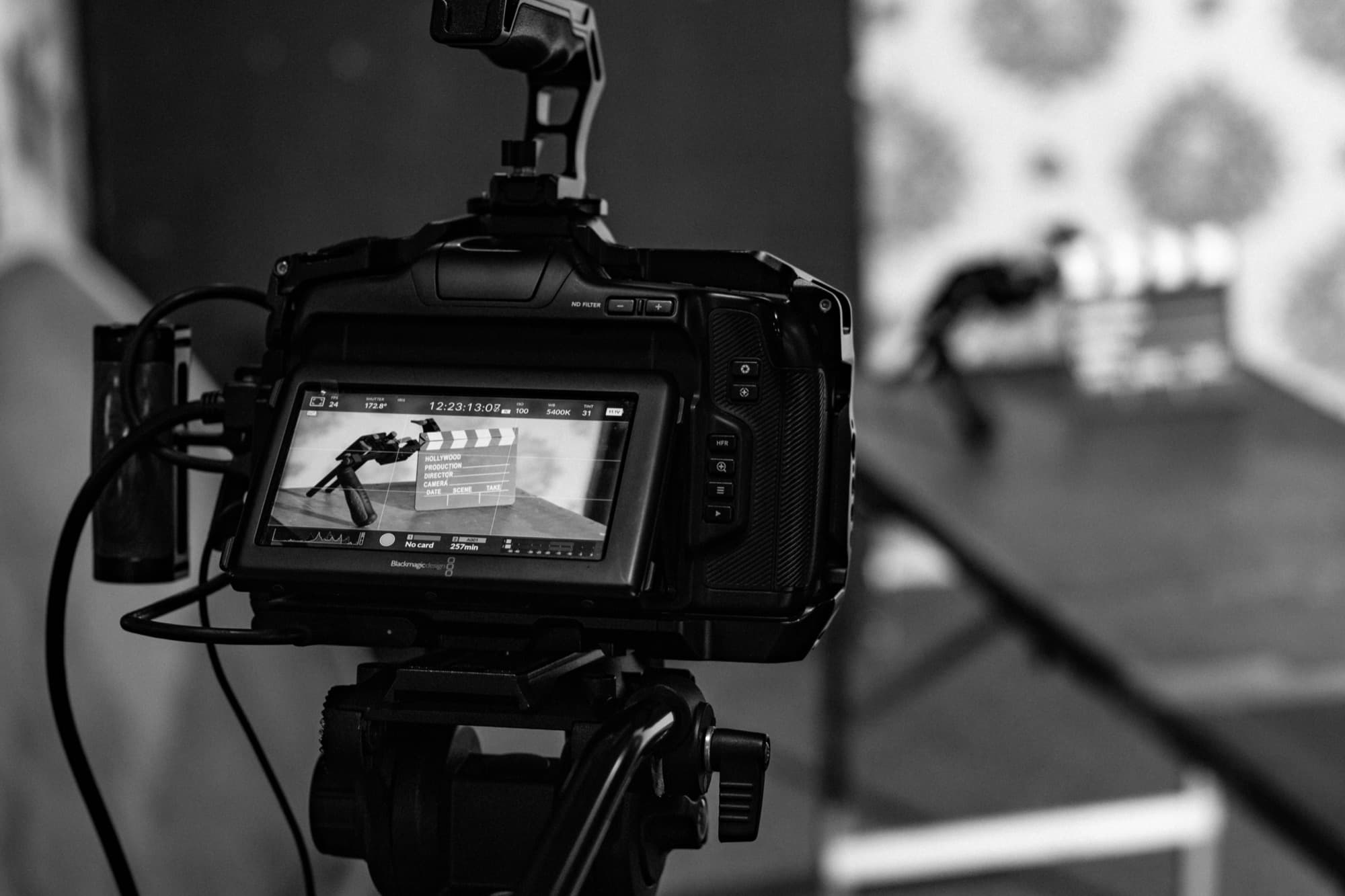 A cinema camera on a tripod, its monitor showing a clapperboard on set